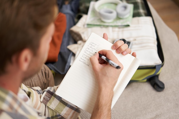 ノートに手書きでメモを取る男性と、後ろに開いたスーツケース